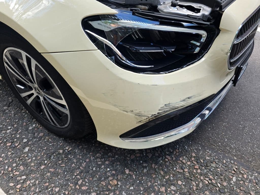 Beschädigte Frontschürze und zerkratzte Felge eines hellen Mercedes