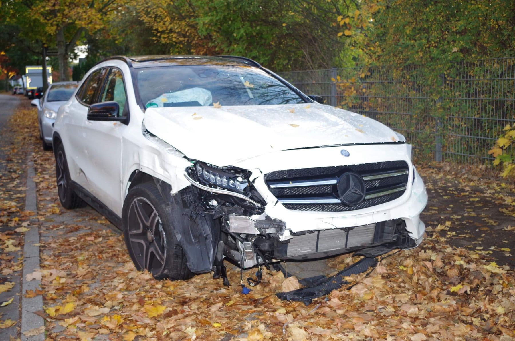 Weißer Mercedes mit schwer beschädigter Front nach einem Unfall, aufgenommen am Standort des Fahrzeugs